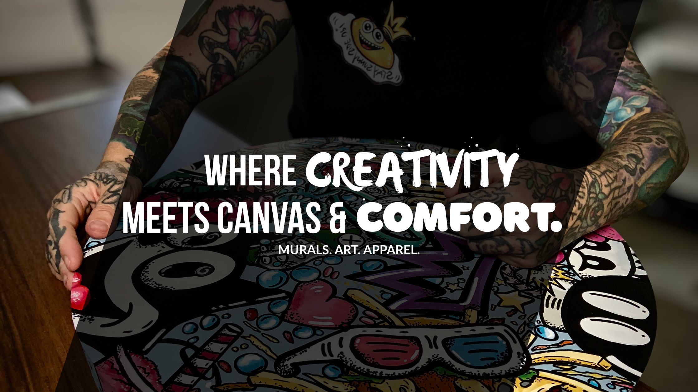 Carly Marie holding a colorful art piece inspired by grafitti and illustrative cartoon with text 'Where creativity meets canvas & comfort' on a blurred background.